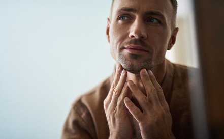 Patient looking in mirror at jawline after dental bridge treatment