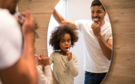 Father and daughter brushing teeth before preventive dentistry visit