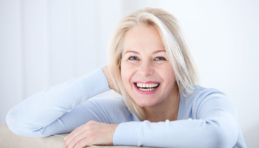 Senior woman in light blue shirt leaning on couch