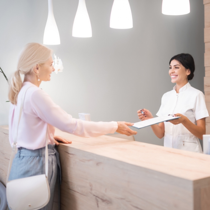 Dental team member greeting patient at dental office reception desk