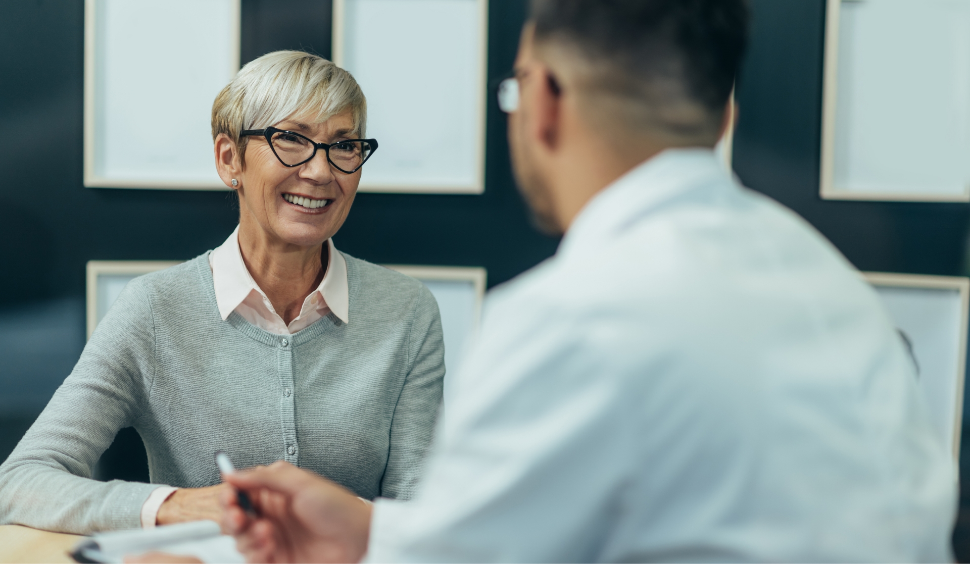 Senior woman smiling while sitting across from her dentist at a desk