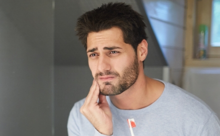 Man looking in mirror and holding his face in pain