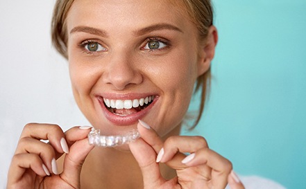 A smiling woman holding a take-home teeth whitening tray