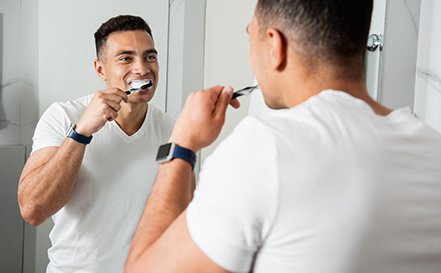 A handsome young man brushing his teeth in front of a bathroom mirror